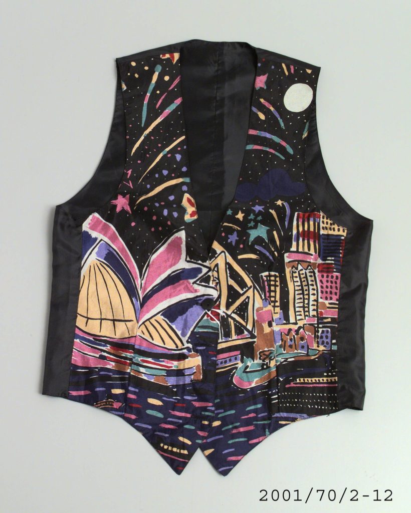 Sleeveless men's waistcoat made of silk and polyester with V-neckline. The front is of colour printed silk featuring the Ken Done design 'Sydney Night'. On a black ground there is the Sydney Opera House, the Sydney Harbour Bridge, boats bobbing on the water and fireworks going off in the sky. The back of the waistcoat is of black polyester and has an adjustable strap with a metal buckle at the waist. The centre front opening fastens with four black plastic buttons. The waistcoat is machine sewn and fully lined with black polyester.